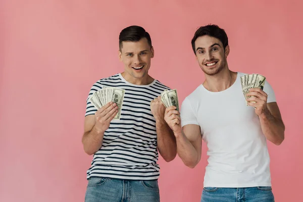 Vista frontal de dos amigos emocionados con billetes de dólar aislados en rosa - foto de stock