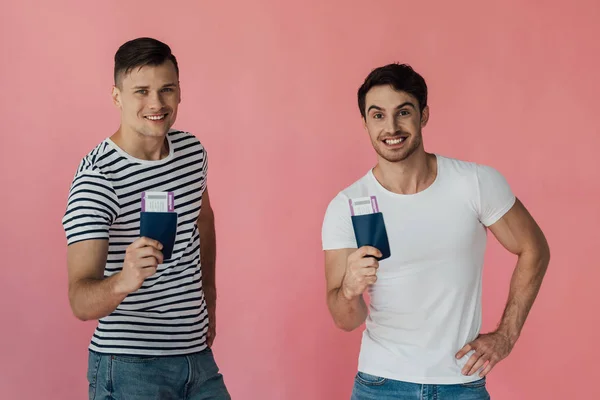 Vista frontal de dos turistas emocionados sonriendo y sosteniendo pasaportes con billetes de avión aislados en rosa - foto de stock
