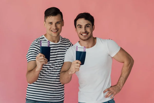 Vista frontal de dois turistas excitados sorrindo e segurando passaportes com passagens aéreas isoladas em rosa — Fotografia de Stock