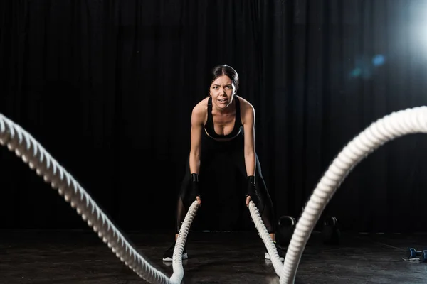 Вибірковий фокус жінки, що вправляється з бойовими мотузками на чорному — стокове фото