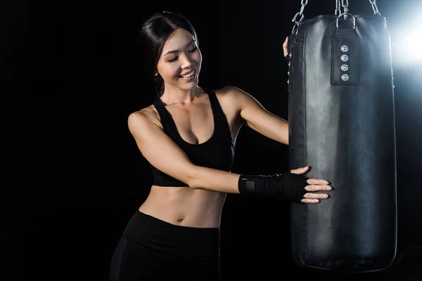 Happy girl looking at punching bag isolated on black — Stock Photo