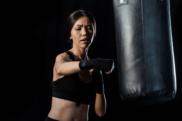 Messa a fuoco selettiva di attraente ragazza lavorando fuori vicino sacco da boxe isolato su nero — Foto stock