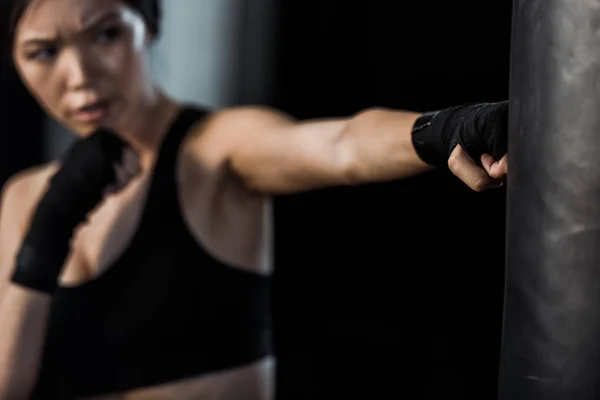 Selective focus of woman working out near punching bag isolated on black — Stock Photo