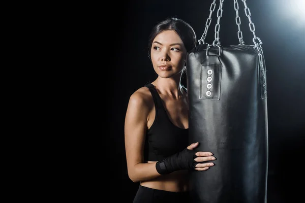 Young woman standing near punching bag isolated on black — Stock Photo