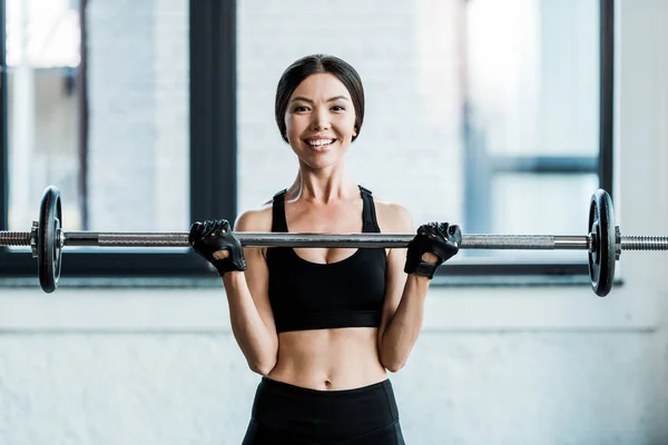 Fröhliche Frau trainiert mit Langhantel im Fitnessstudio — Stockfoto