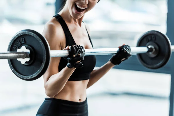 Emotionale junge Frau trainiert mit Langhantel im Fitnessstudio — Stockfoto