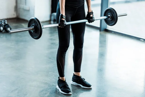 Cropped view of young woman in sportswear working out with barbell in gym — Stock Photo