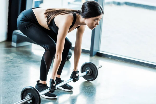 Целенаправленная молодая женщина в спортивной одежде, упражняющаяся с штангой в спортзале — стоковое фото
