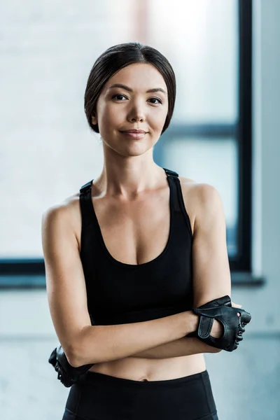 Happy young woman in gloves standing with crossed arms — Stock Photo