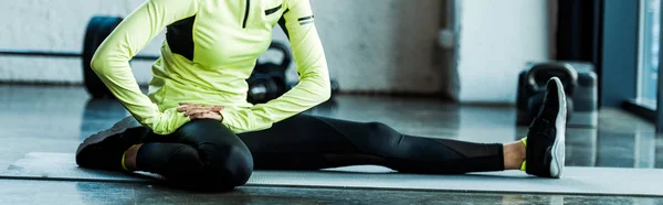 Colpo panoramico di giovane donna in abbigliamento sportivo che si allunga sul tappeto fitness in palestra — Foto stock