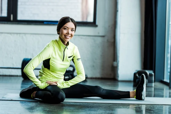 Jovem mulher alegre alongamento no tapete de fitness no ginásio — Fotografia de Stock