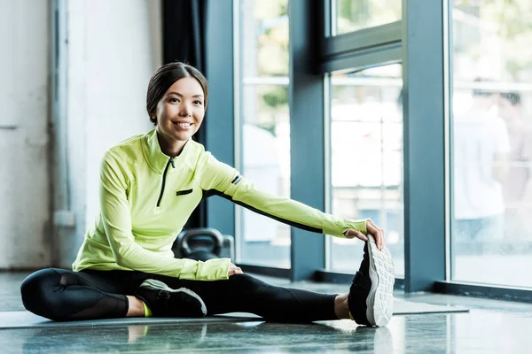 Весела молода жінка тягнеться на фітнес килимок у спортзалі — стокове фото