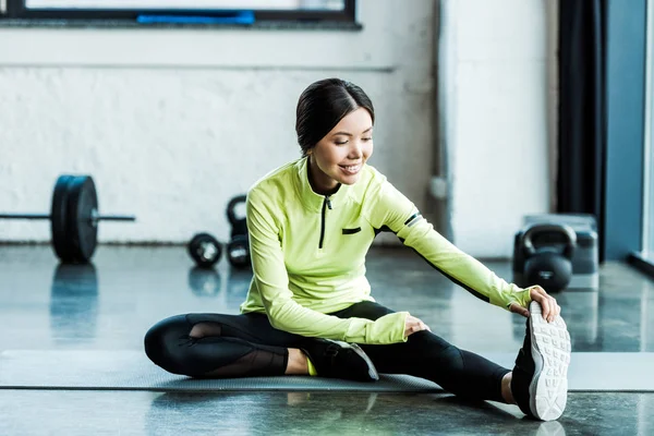 Feliz joven en ropa deportiva estiramiento en el gimnasio - foto de stock