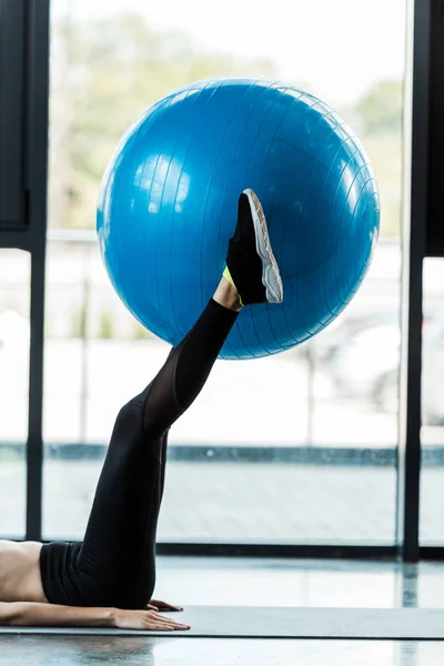 Vista ritagliata di ragazza che esercita con palla fitness blu sul tappeto fitness — Foto stock