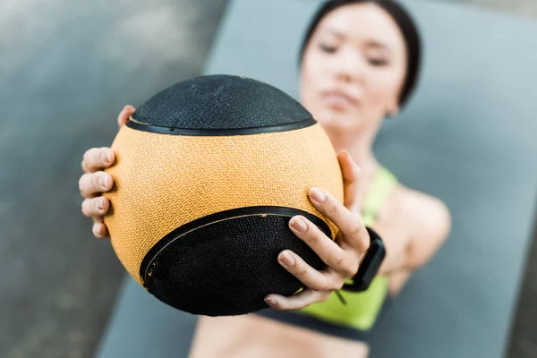 Selective focus of young woman holding ball while lying on fitness mat — Stock Photo