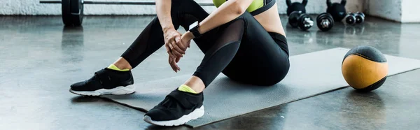 Panoramic shot of woman sitting on fitness mat near ball — Stock Photo