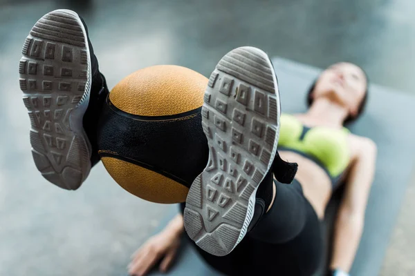 Focalizzazione selettiva della donna che si allena con la palla sul tappeto fitness in palestra — Foto stock