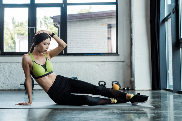 Tired girl in sportswear sitting on fitness mat in gym — Stock Photo