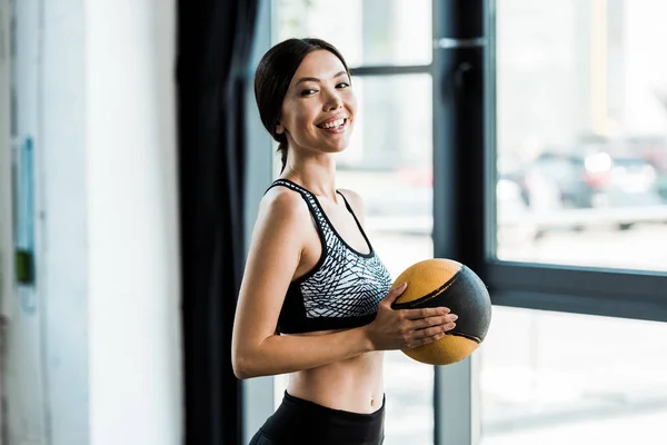Счастливая женщина, держащая желтый мяч и улыбающаяся в спортзале — стоковое фото
