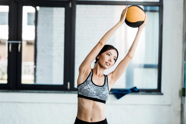 Atractiva joven deportista sosteniendo la pelota mientras hace ejercicio en el gimnasio - foto de stock
