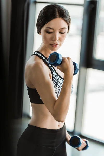 Jeune femme sportive regardant haltères tout en travaillant dans la salle de gym — Photo de stock