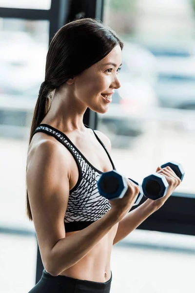 Mujer positiva y deportiva sosteniendo pesas en el gimnasio - foto de stock