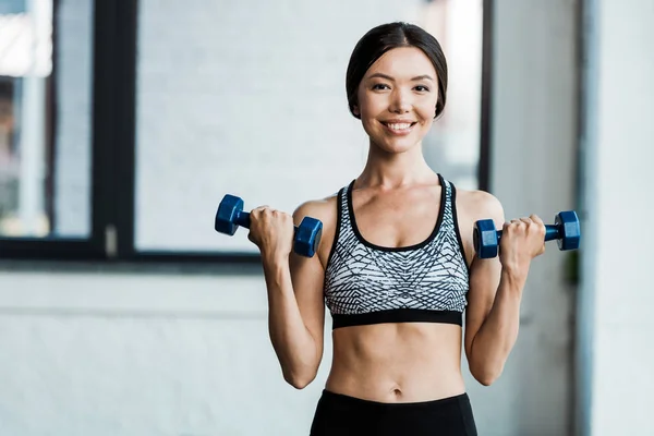 Donna felice e sportiva che tiene i manubri in palestra — Foto stock