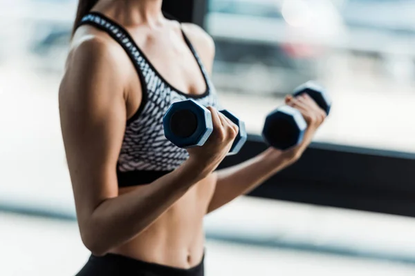 Vue recadrée de fille sportive tenant des haltères dans la salle de gym — Photo de stock