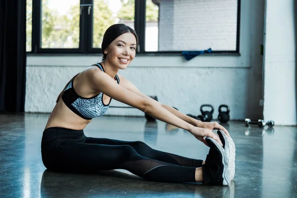 Junge Sportlerin dehnt sich und lächelt im Fitnessstudio — Stockfoto