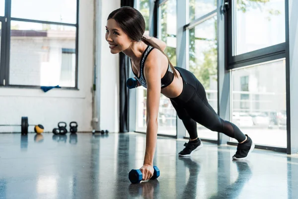 Fille heureuse exercice avec haltères dans le centre sportif près des fenêtres — Photo de stock