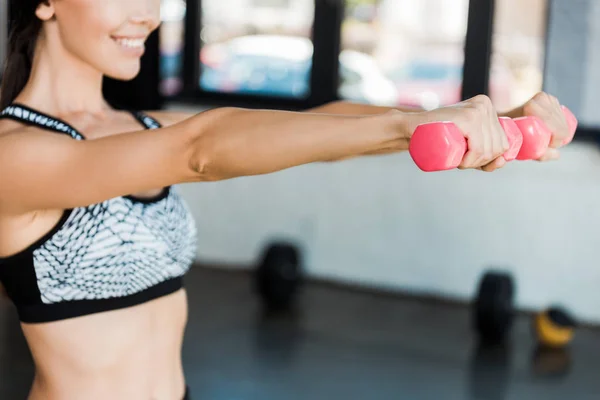 Cropped view of happy girl holding pink dumbbells while exercising in gym — Stock Photo