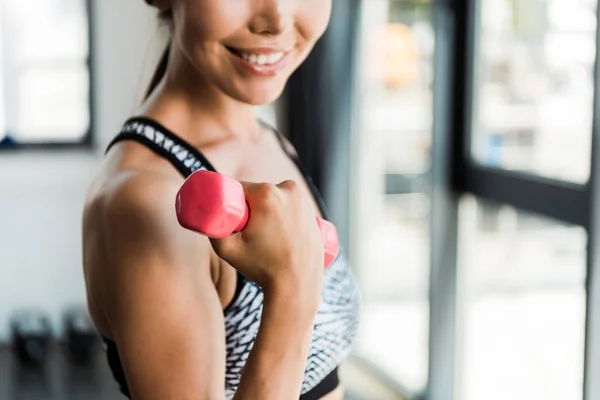 Cropped view of happy girl holding pink dumbbell in gym — Stock Photo