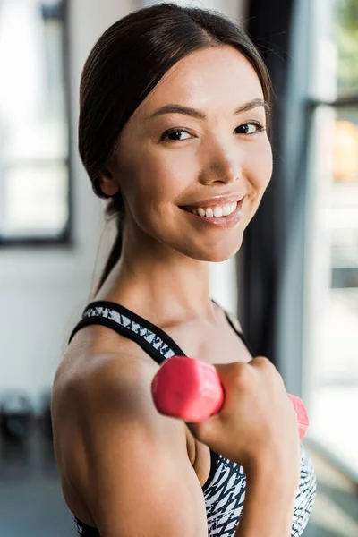 Selective focus of happy girl holding pink dumbbell while looking at camera — Stock Photo