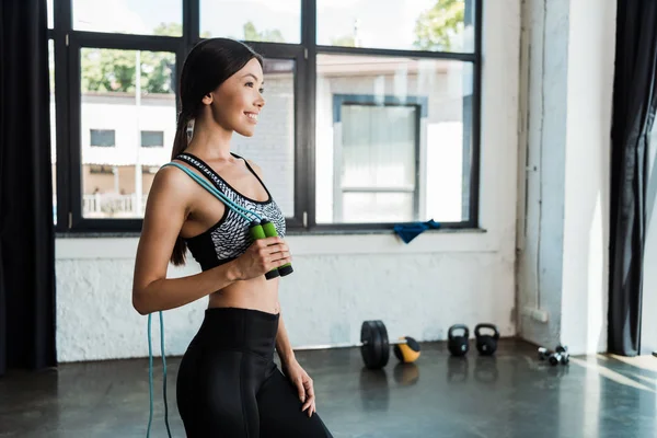 Happy woman holding jumping rope while standing in gym — Stock Photo