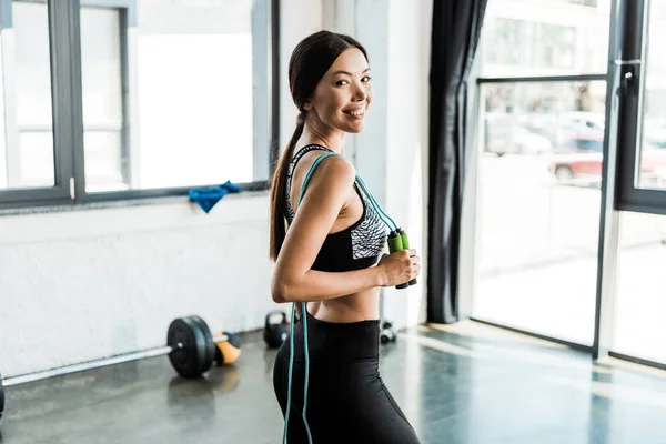 Femme sportive heureuse tenant corde sautante tout en se tenant dans la salle de gym — Photo de stock