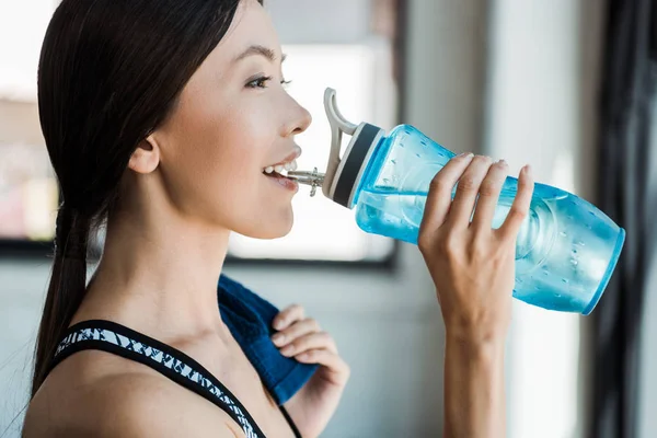 Feliz mujer beber agua mientras sostiene deporte botella - foto de stock