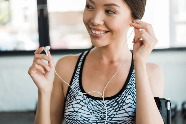 Mujer atlética positiva sosteniendo auriculares en el gimnasio - foto de stock