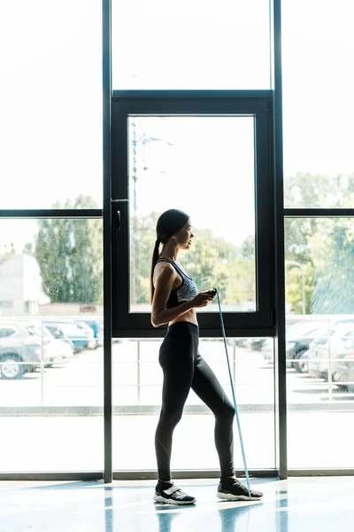 Vista lateral de atraente jovem mulher exercitando com pular corda — Fotografia de Stock