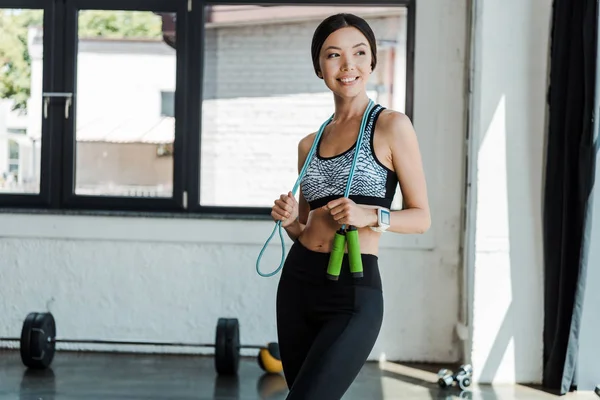 Joyeuse jeune femme souriante tout en tenant la corde sautante dans la salle de gym — Photo de stock