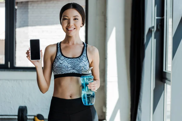 Весела дівчина тримає спортивну пляшку і смартфон з порожнім екраном — стокове фото