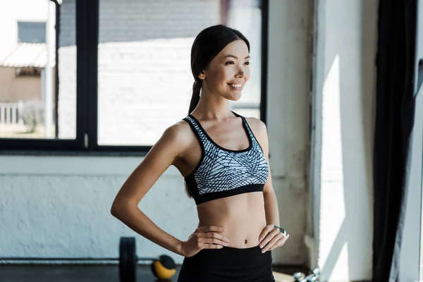 Cheerful young woman standing with hands on hips in gym — Stock Photo