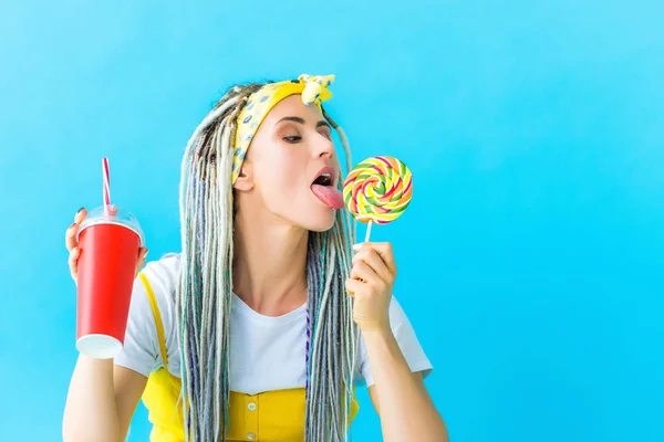 Girl with dreadlocks and soda drink licking lollipop isolated on turquoise — Stock Photo