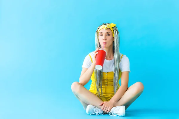 Belle fille avec dreadlocks assis et boire soda sur turquoise — Photo de stock