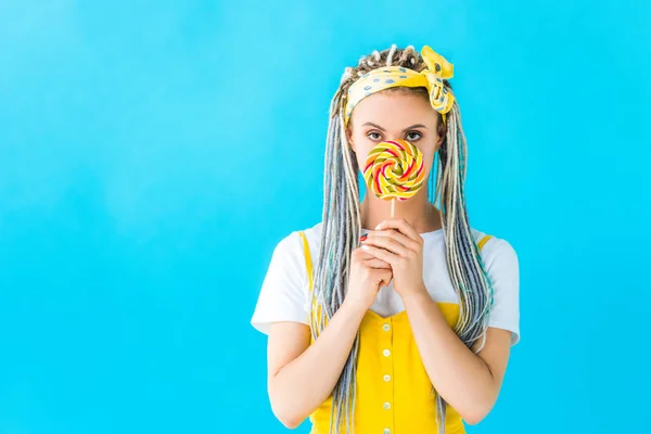 Beautiful girl with dreadlocks covering face with lollipop isolated on turquoise — Stock Photo