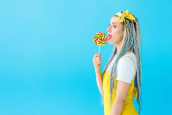 Side view of attractive girl with dreadlocks licking lollipop isolated on turquoise — Stock Photo