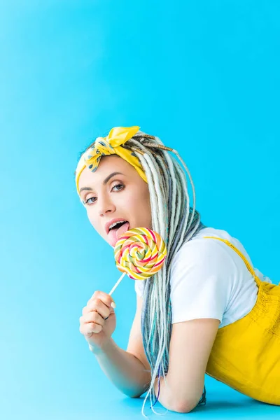 Girl with dreadlocks licking lollipop on turquoise — Stock Photo