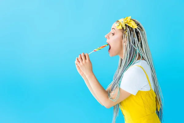 Side view of girl with dreadlocks eating lollipop isolated on turquoise — Stock Photo