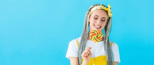 Tiro panorâmico de menina feliz com dreadlocks segurando pirulito isolado em turquesa — Fotografia de Stock