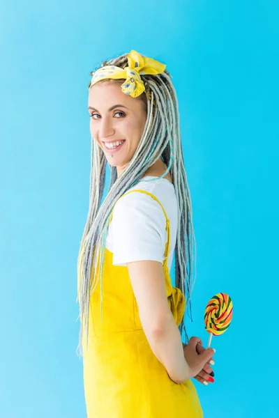 Fille souriante avec dreadlocks regardant caméra tout en tenant sucette isolé sur turquoise — Photo de stock