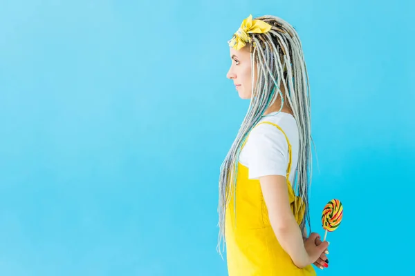 Vista lateral da menina com dreadlocks segurando pirulito isolado em turquesa com espaço de cópia — Fotografia de Stock